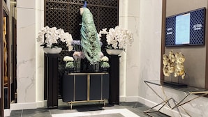 En moderne lobby med en påfugludsstilling, hvide orkideer, et sort konsolbord og en gylden skulptur.