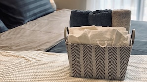 En pænt redt seng med en grå og hvidstribet pude, et beige pled og en kurv med et mønster på sengen.