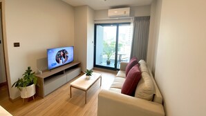 En moderne stue med et fladskærms-tv, en sofa, et sofabord og en potteplante.