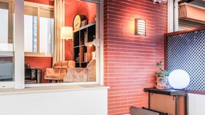 Una sala de estar moderna con una pared de ladrillo rojo, un ventanal grande y un área de descanso con un sofá blanco y dos sillones.