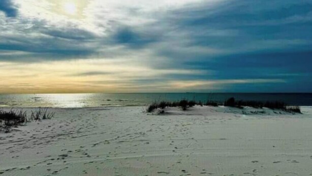 A beach with footprints, a clear sky, and the sun setting or rising.