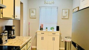 A kitchen with a countertop, cabinets, a stove, a refrigerator, and a window with blinds.