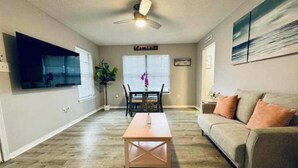 A living room with a wooden coffee table, a sofa, a ceiling fan, and a dining area with a table and chairs.