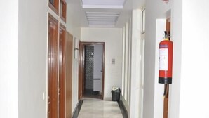 A hallway with a tiled floor, wooden doors, a fire extinguisher, and a ceiling light fixture. - Hotel Apple Inn (Nainital)