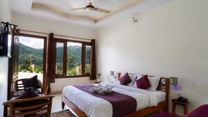 A bedroom with a bed, a chair, a ceiling fan, a TV, and a view of the outdoors. - Hotel Apple Inn (Nainital)