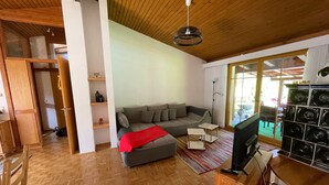 A living room with a wooden ceiling, a grey sofa, a television, and a wooden cabinet.