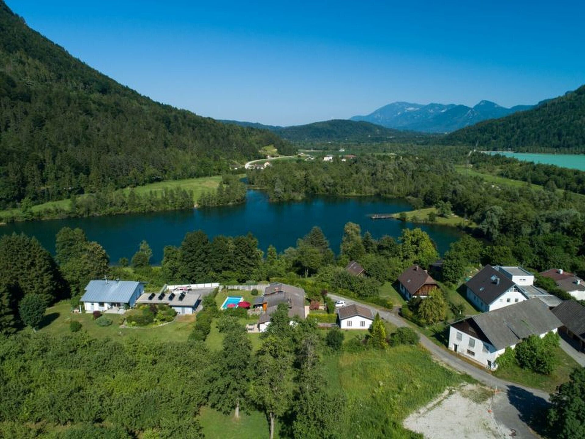 Una propietat a la vora d'un llac amb diverses cases, una piscina i un paisatge forestal.