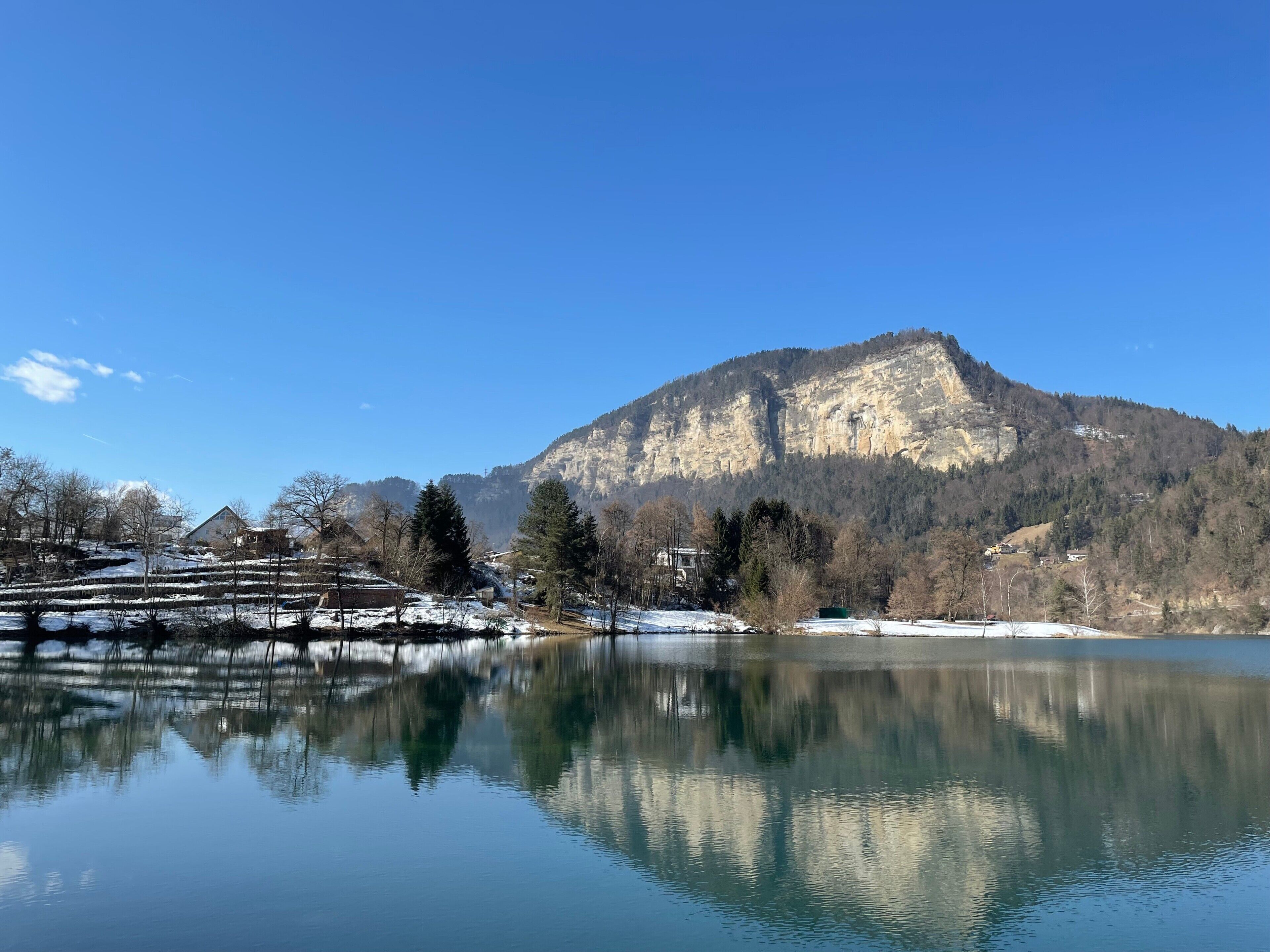 Une montagne avec un lac au premier plan, des arbres et un bâtiment.