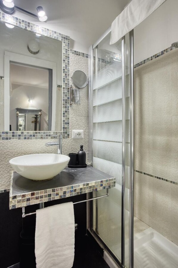 Un baño moderno con un lavabo blanco, un espejo grande y una cabina de ducha de vidrio.
