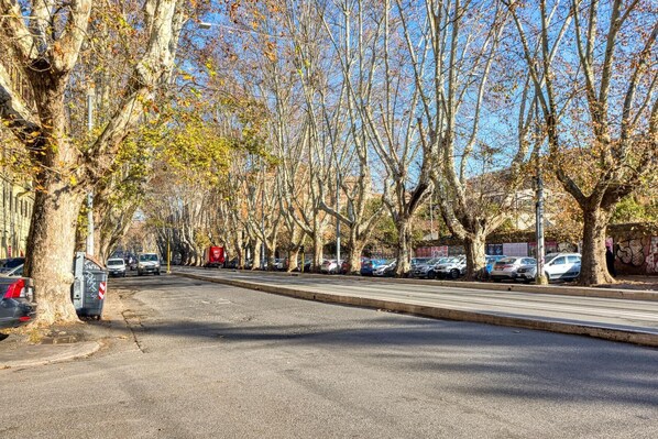 Une rue bordée d’arbres, avec des voitures garées et un ciel dégagé.