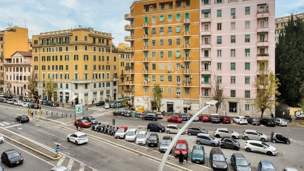 A multi-story residential building with balconies, a parking lot, and a street with cars.