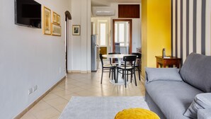 A living room with a grey sofa, a yellow ottoman, and a dining area with a round table and chairs.
