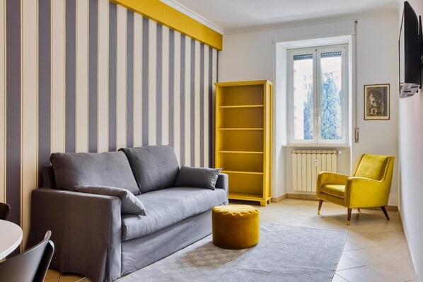A living room with a sofa, ottoman, yellow armchair, and a bookshelf. - Yellow Stripes Apartment - St. John's by RHR (ROMA)