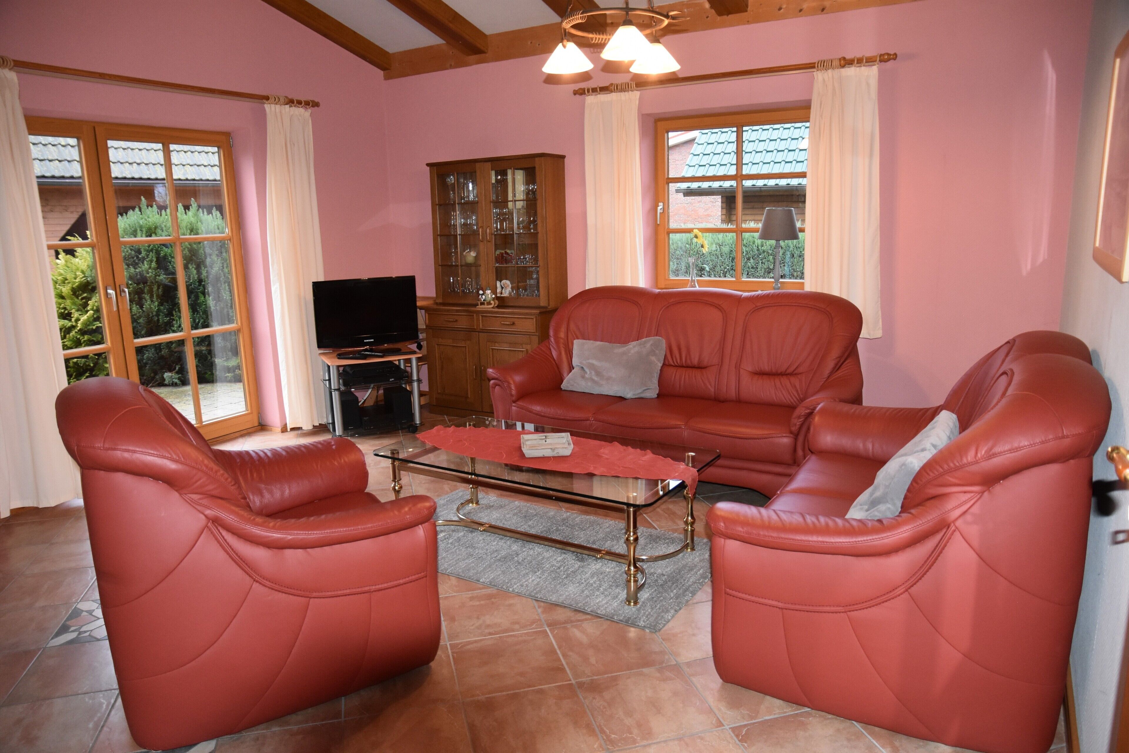 A living room with a red leather sofa, a glass coffee table, and a wooden cabinet.