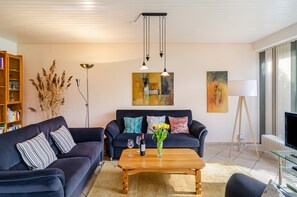 Een moderne woonkamer met een bank, salontafel, boekenkast, kunstwerk en een televisie.