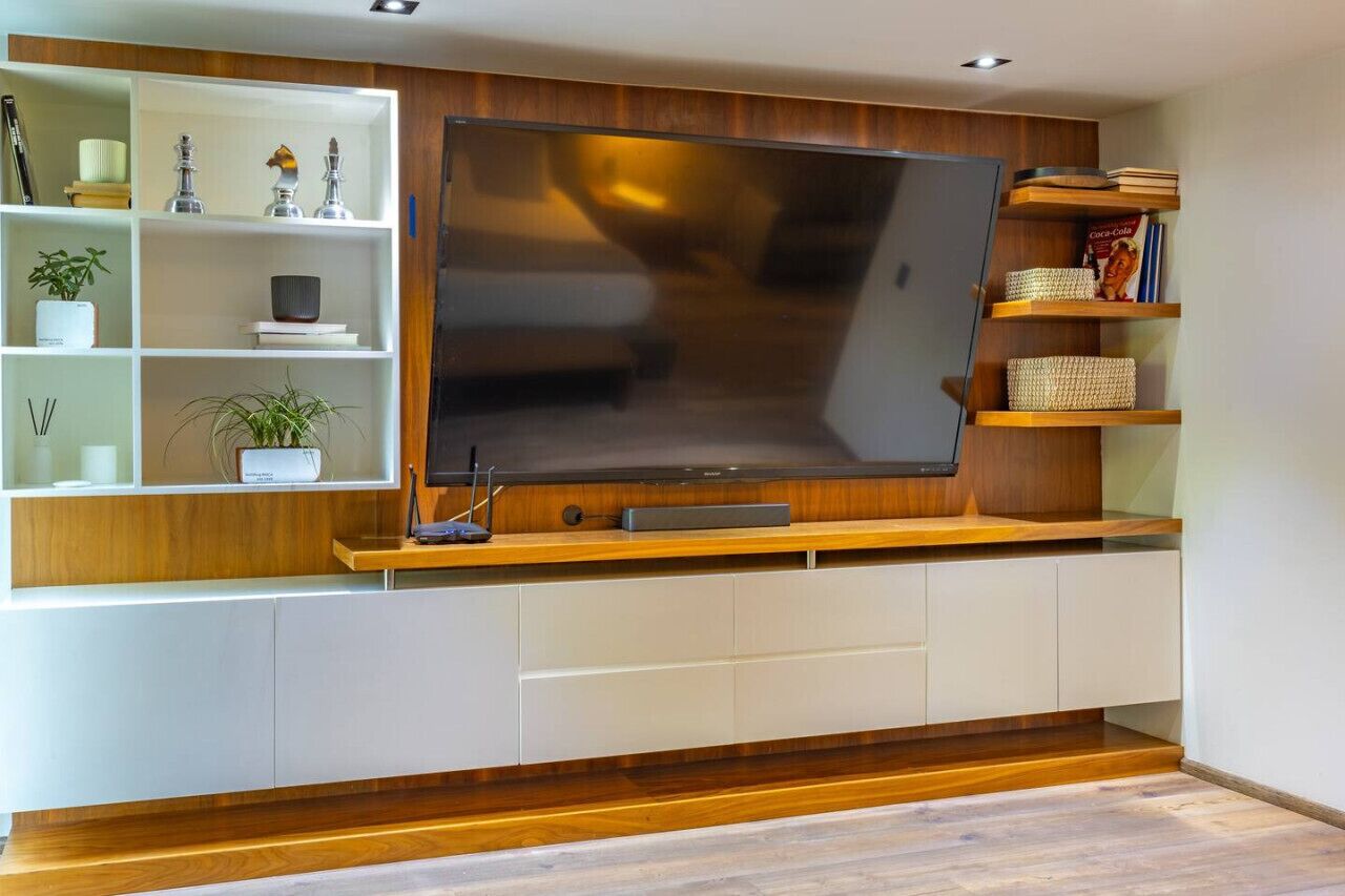 Un salon moderne avec un grand téléviseur à écran plat fixé à un mur en bois, des étagères intégrées ornées d’objets décoratifs et un meuble blanc en dessous.
