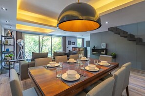 Uma sala de jantar moderna com uma mesa grande posta para quatro pessoas, uma luminária de teto singular e uma escada à direita.
