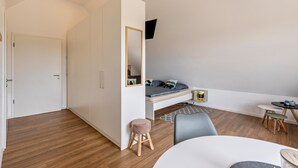 A modern bedroom with a loft bed, a small stool, a round table, and a TV mounted on the wall.