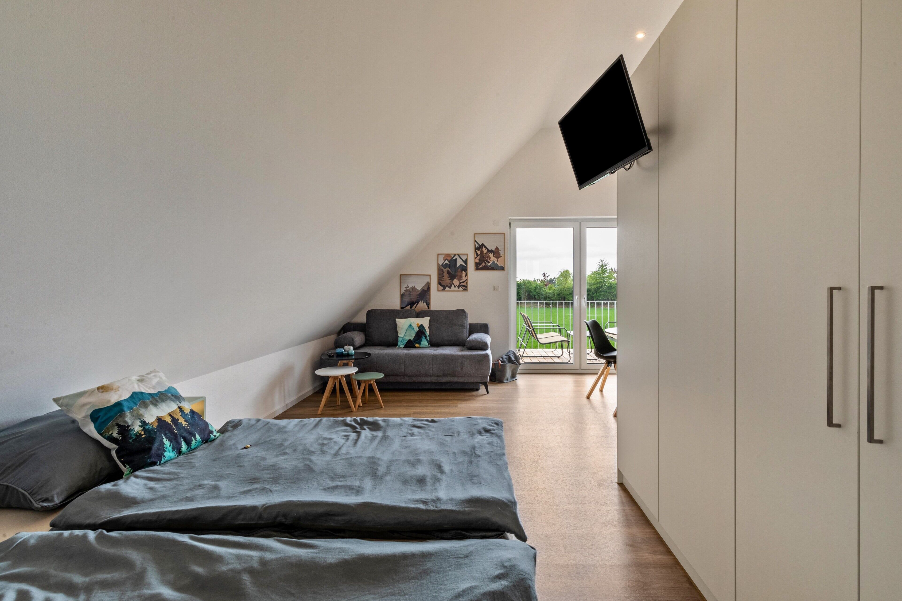 Et moderne soveværelse med seng, sofa, tv og en skydedør til en balkon.