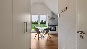 A modern kitchen with a dining area, a large sliding glass door to a balcony, and a view of greenery.