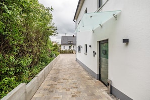 A pathway leading to a building with a glass entrance, surrounded by greenery.