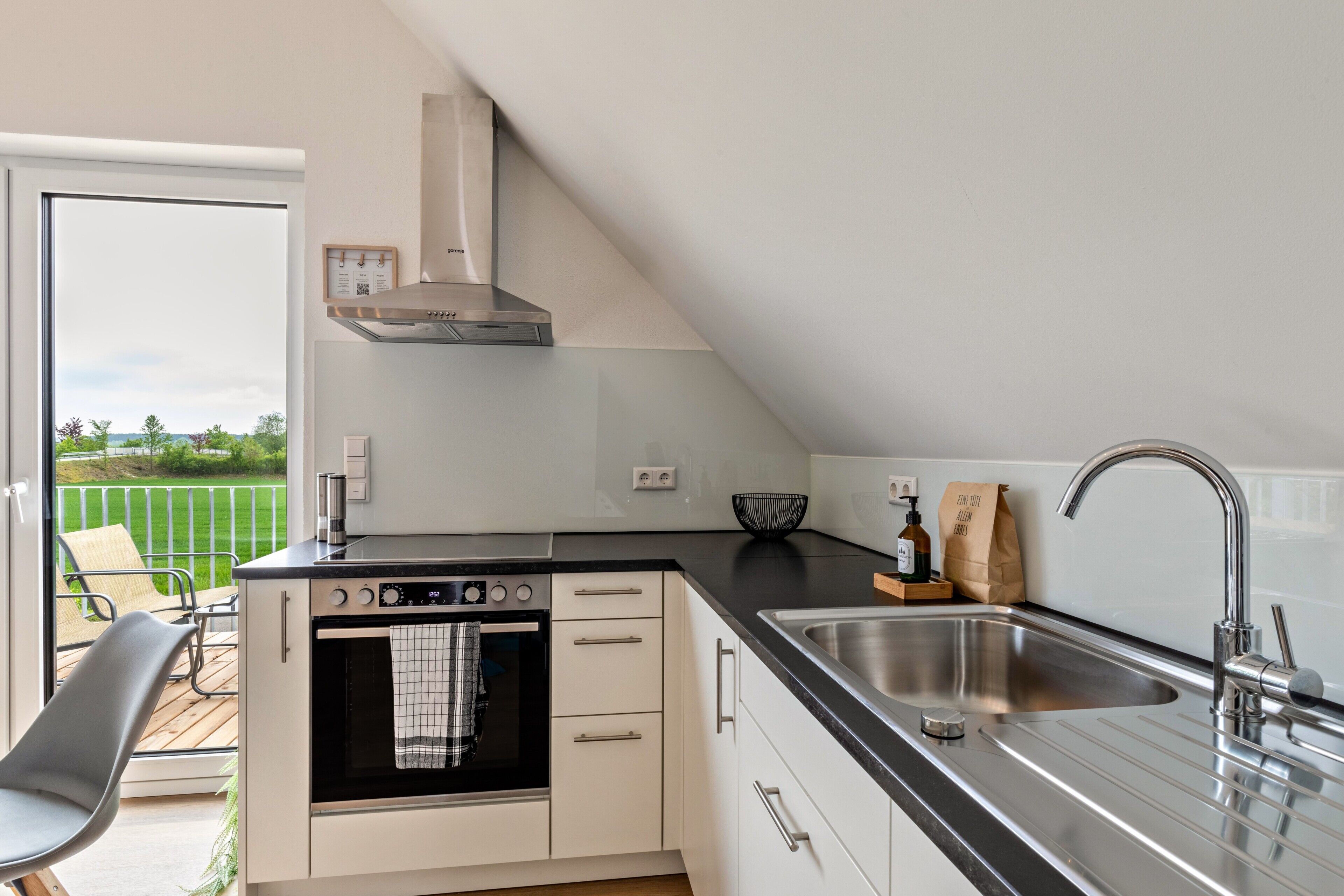 Eine moderne Küche mit Backofen, Spüle aus Edelstahl und Blick auf eine grüne Außenanlage.