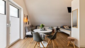 Una camera da letto mansardata moderna con una grande finestra, un tavolo da pranzo rotondo e un angolo salotto accogliente.