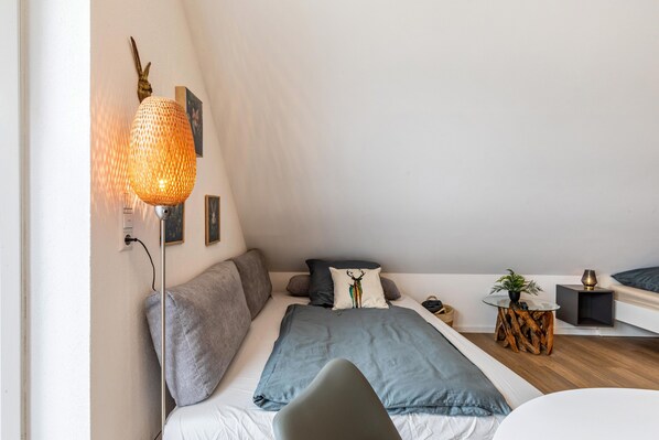Quarto moderno com cama, mesas de cabeceira, abajur e prateleira na parede.