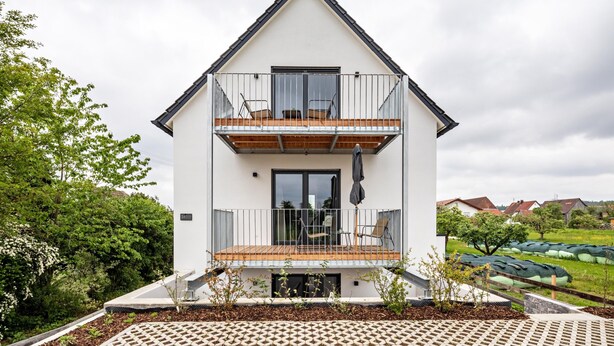 Una casa a due piani con un balcone, un ponte in legno e vista sul paesaggio circostante.