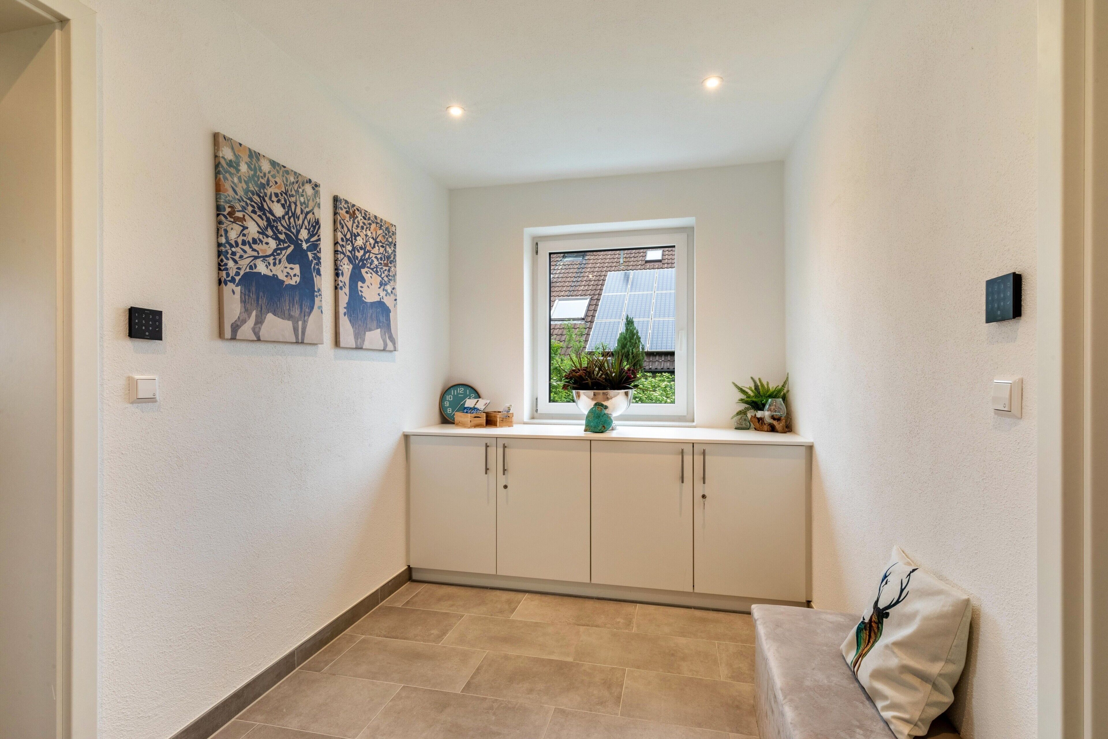 Um corredor com um banco embutido, uma janela com vista para vegetação e duas pinturas de veados penduradas na parede.