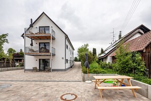 Ein zweistöckiges Haus mit Balkon, einer Terrasse mit Tisch und Stühlen sowie einem Garten.