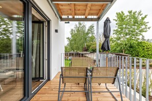 Ein Balkon mit zwei Korbstühlen, einem Tisch und einer Holzbalkendecke.