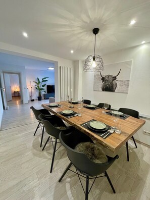 A dining area with a wooden table set for six, black chairs, a pendant light, and a bull-themed artwork on the wall. - Apartment 'Casa Schneck' with Private Terrace and Wi-Fi (Longkamp)
