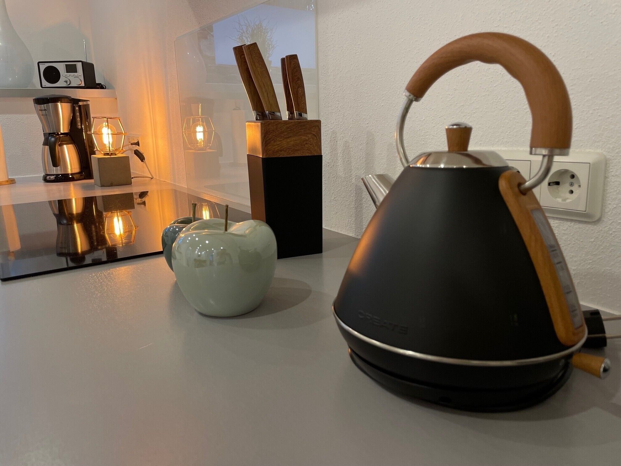 A modern kitchen with a kettle, a coffee maker, and a decorative apple.
