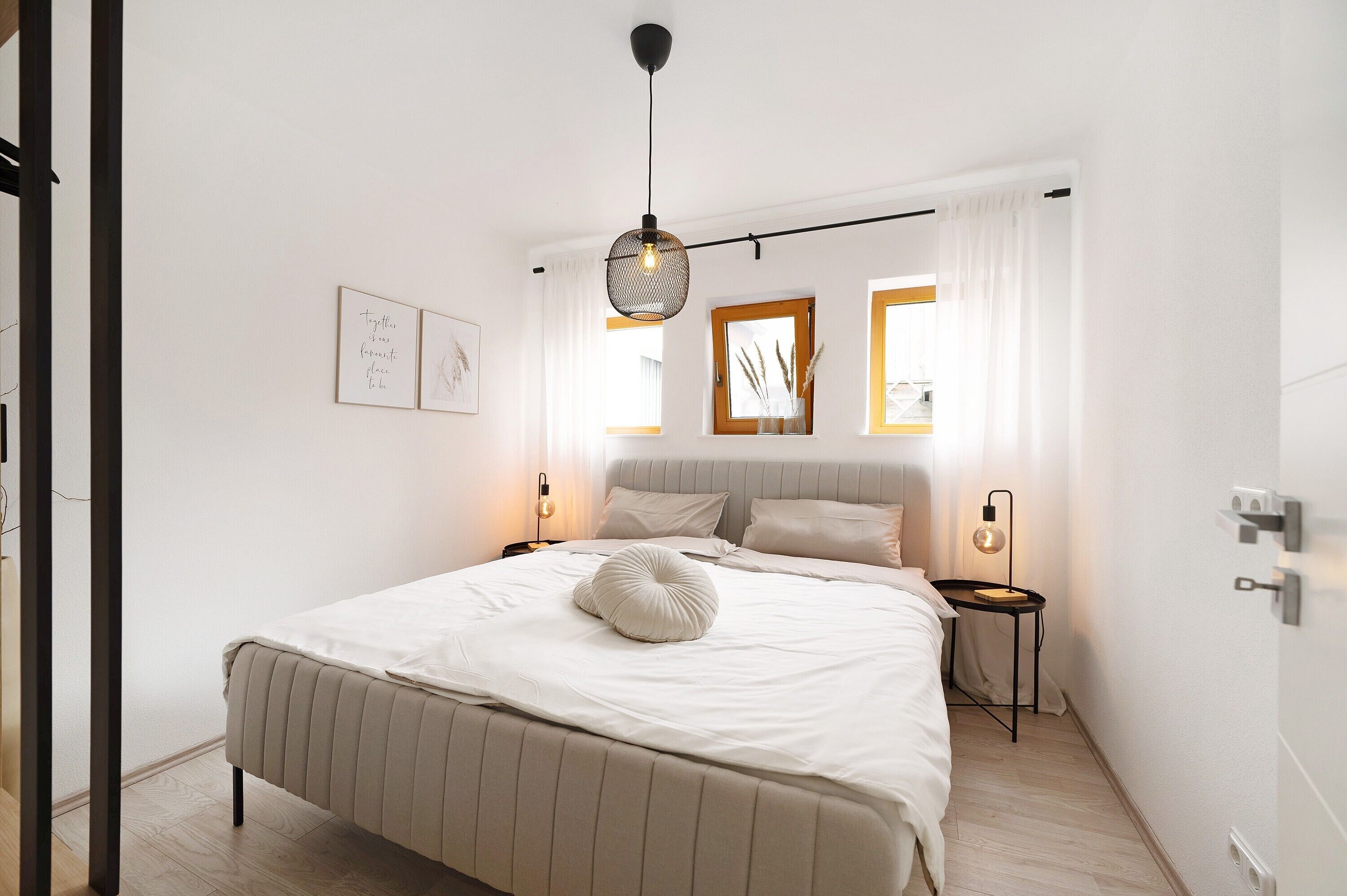 A bedroom with a bed, bedside tables, a hanging light fixture, and framed artwork on the wall.
