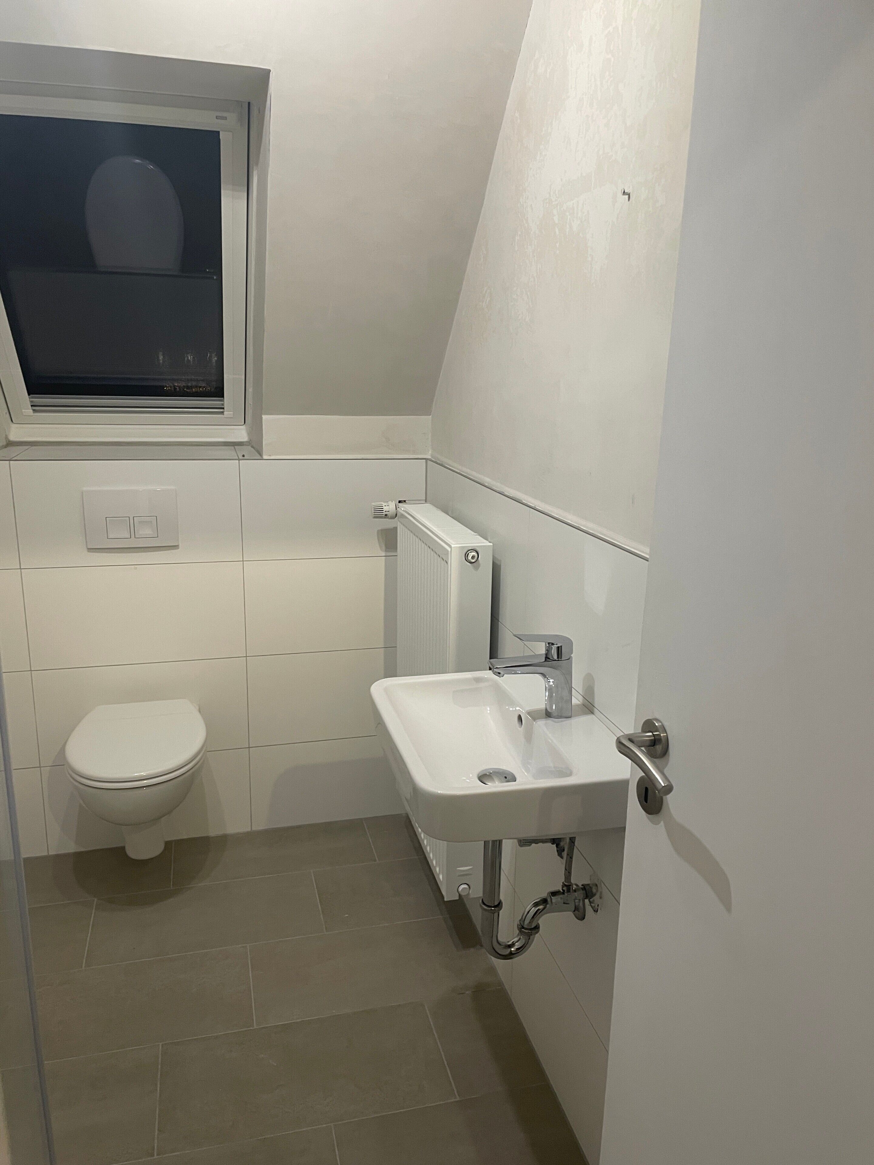 A small, modern bathroom with a toilet, a window, a radiator, and a sink.