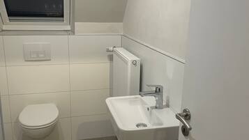 A small, modern bathroom with a toilet, a window, a radiator, and a sink.