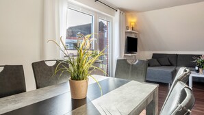 Un salon moderne comprenant une table à manger, des chaises, un canapé et un téléviseur.