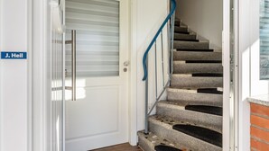 Un escalier avec une rampe métallique, une porte blanche dotée d’une vitre en verre dépoli et une plaque nominative portant l’inscription « J. Heil ».
