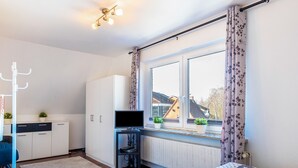 Une chambre à coucher avec un lit, une télévision, une armoire, un radiateur et une fenêtre avec des rideaux.