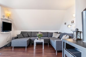 Ein modernes Wohnzimmer mit einer Eckcouch, einem Flachbildfernseher, einem kleinen Tisch mit einer Vase und einer dekorativen Laterne.