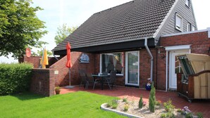 A brick house with a covered patio, a dining area with chairs and a table, and a small garden.