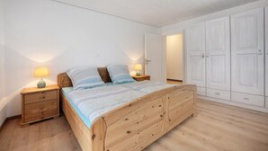 Una camera da letto con un letto in legno, due comodini con lampade, un armadio e una porta che dà su un'altra stanza.