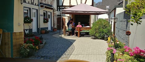 A courtyard with a wooden bench, potted plants, and a building with a sloped roof.