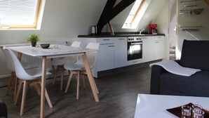A modern kitchen with white cabinets, a black countertop, and a built-in oven. There is a dining area with a white table and chairs, and a grey sofa in the living area. - Holiday Apartment 'Rheinblick Wohnung 5' with Shared Terrace, Wi-Fi and Air Conditioning (Koblenz)