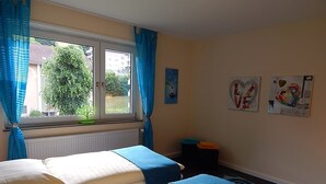 Ein Zimmer mit zwei Betten, einem Vorhangfenster, einem Heizkörper und Bildern an der Wand.