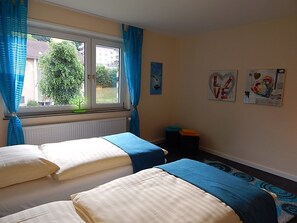 Een kamer met twee bedden, een raam met gordijnen, een radiator en kunst aan de muur.