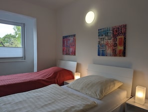 Une chambre avec deux lits, une fenêtre et des œuvres d’art murales.