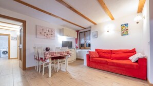 A compact living space with a dining area, a red sofa, and a kitchen. - Beautiful, recently renovated flat (Canazei)