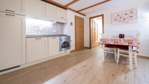 A kitchen with white cabinets, a stainless steel oven, and a wooden ceiling. - Beautiful, recently renovated flat (Canazei)